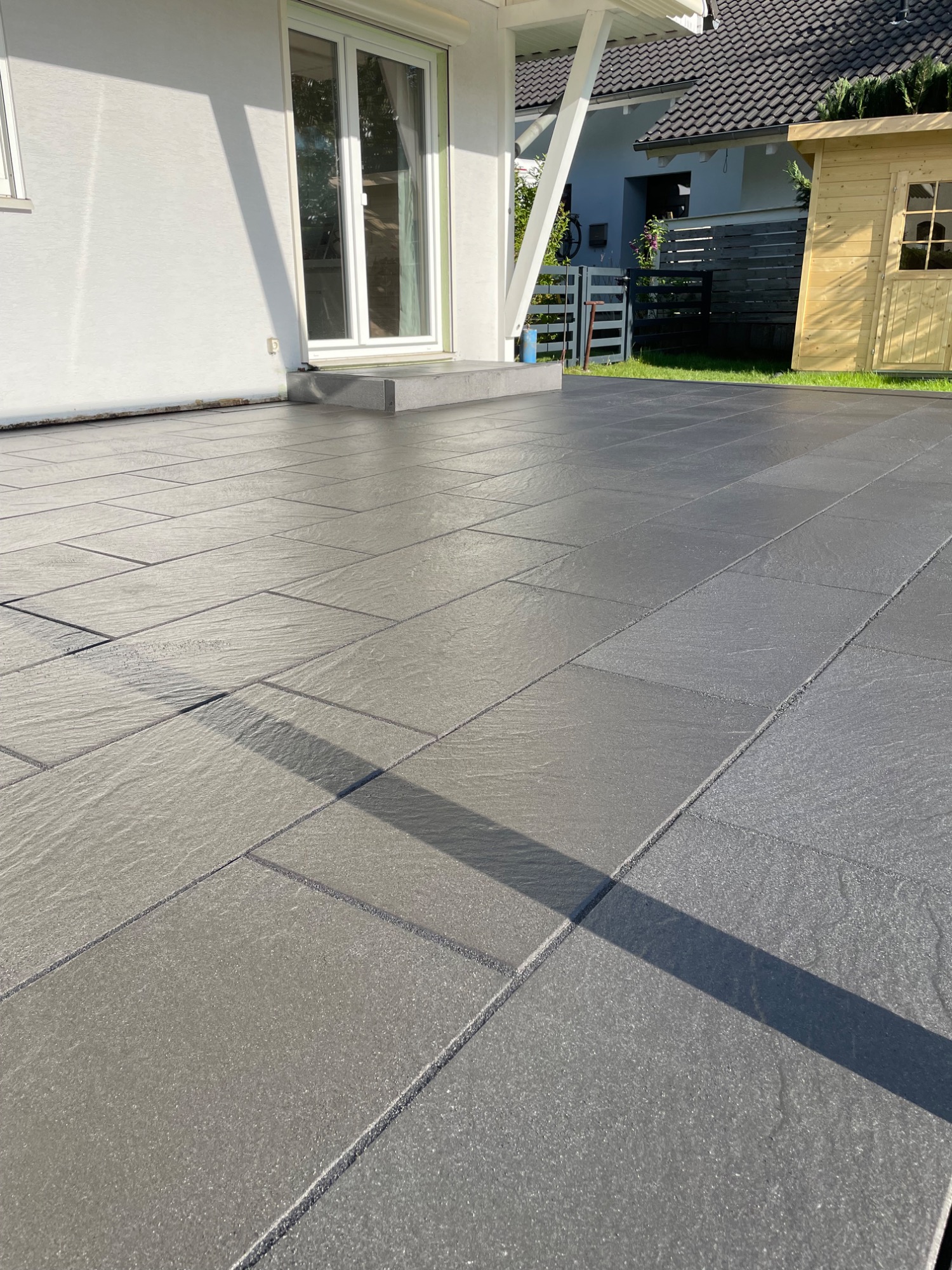 Glatte, graue Fliesen auf einem Terrassenboden mit Schattenwurf.