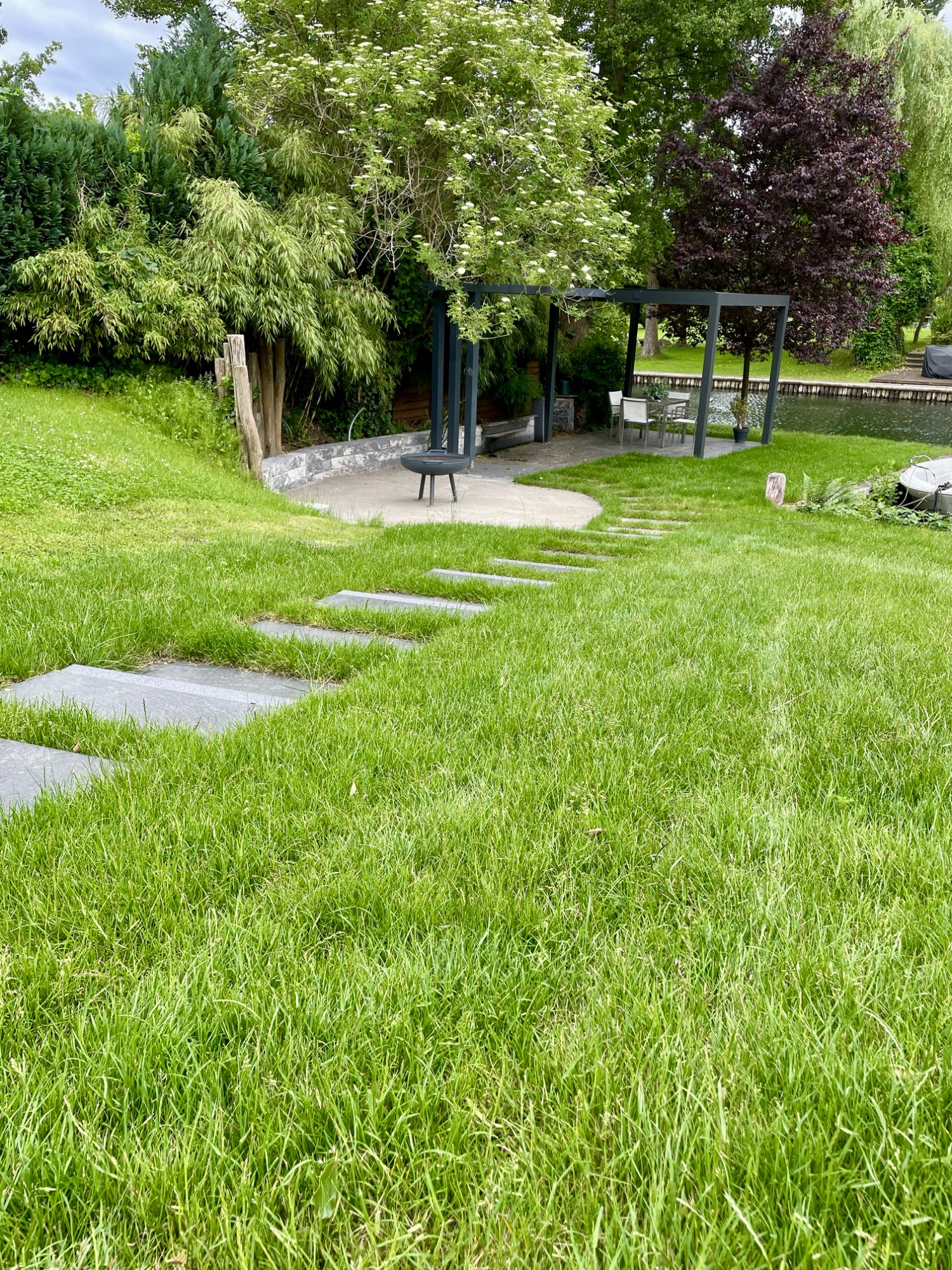Grüner Garten mit Rasen, Steinplatten und einer geselligen Sitzgelegenheit im Hintergrund.