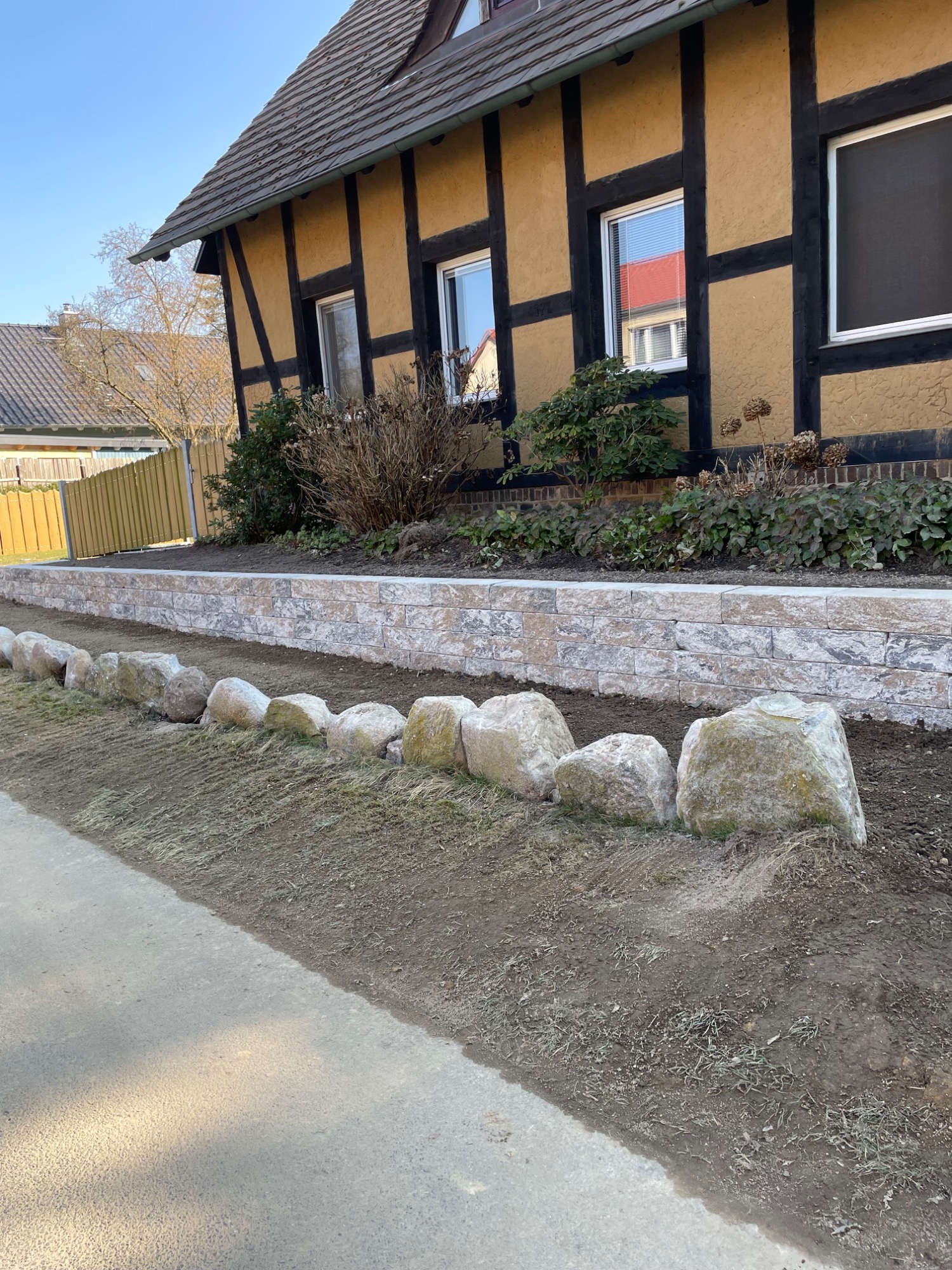 Eine Steinmauer umgeben von Rasen neben einem Fachwerkhaus.