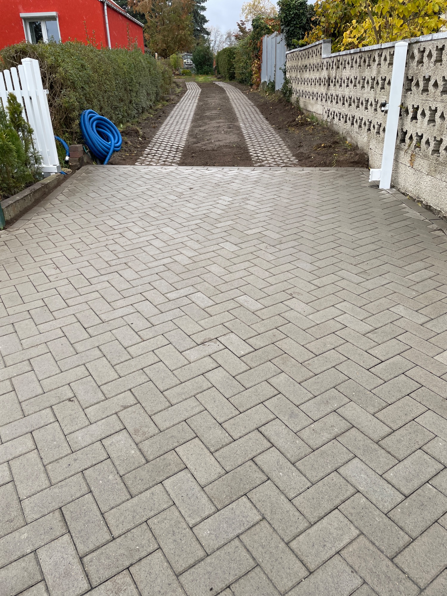 Gepflasterte Auffahrt mit einem Weg zwischen Büschen und einer roten Wand.