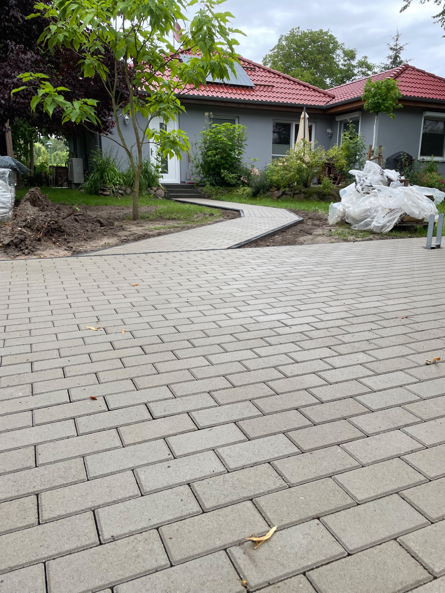 Gepflasterter Weg zu einem Haus mit Rasen und Bäumen im Hintergrund.