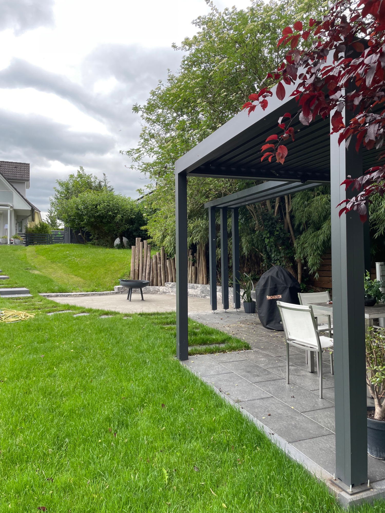 Moderner Pavillon mit Terrasse in einem grünen Garten, bewölkter Himmel im Hintergrund.